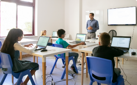 Pupils on computers listening to a teacher
